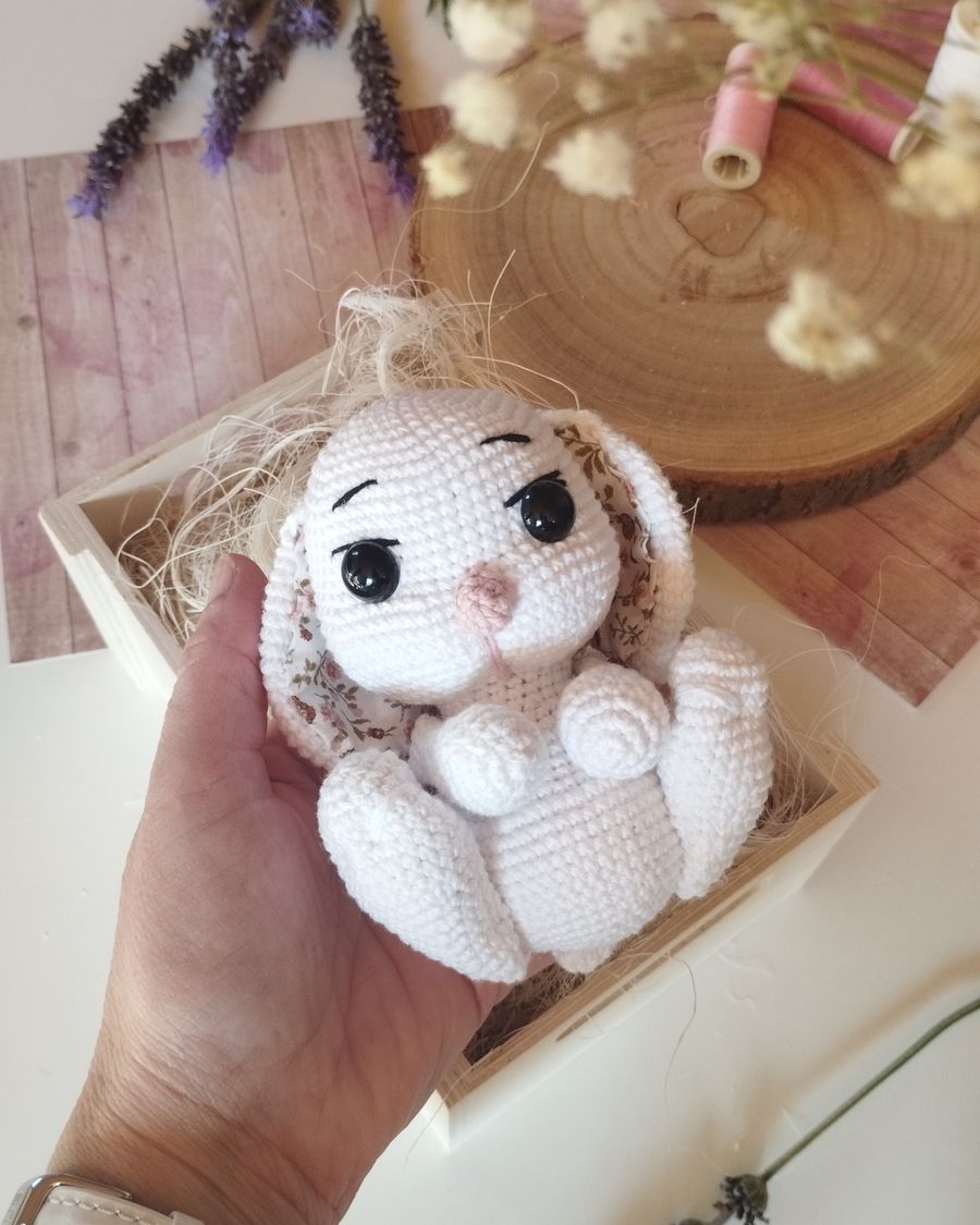 A small cream amigurumi bunny with long ears sitting on a stack of books